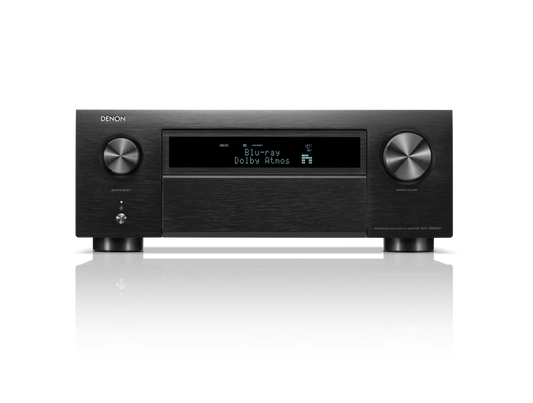Frontansicht des Denon AVC-X6800H AV-Receivers in Schwarz mit großen Lautstärke- und Eingangsknöpfen, Display mit Blu-ray Dolby Atmos, HEOS® Built-in Logo sowie diversen Bedientasten. Das Gerät spiegelt sich auf einer glänzenden Oberfläche.