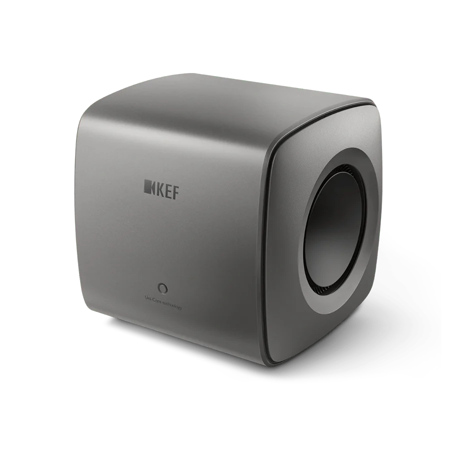 Der KEF KC62 Subwoofer in Titanium Grey besticht durch sein minimalistisches Design mit abgerundeten Kanten, einem Logo auf der Vorderseite und einem runden Seitenlautsprecher.