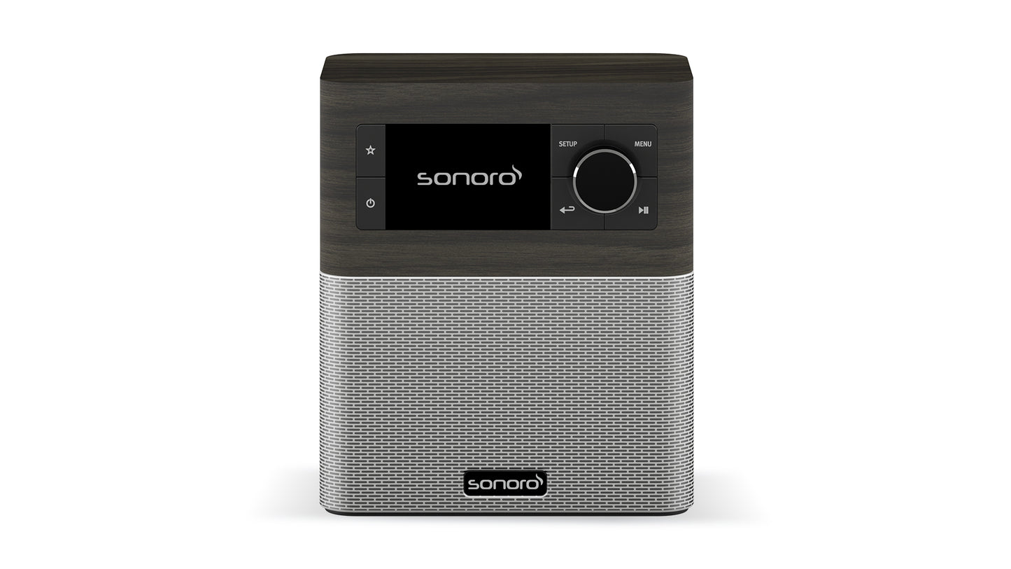 Das Sonoro Stream in Mooreiche (dekor) - Silber ist ein rechteckiges DAB+-Digitalradio mit Bedientasten und einem schwarzen Display auf der Oberseite sowie einem silbernen Lautsprechergitter darunter. Das Sonoro-Logo erscheint sowohl auf dem Bildschirm als auch auf dem Gitter.