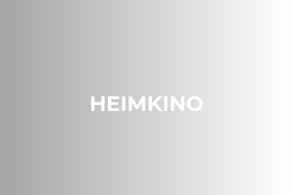 Der weiße Text HEIMKINO steht mittig auf einem Hintergrund mit Farbverlauf, der von Dunkelgrau auf der linken Seite zu Hellgrau auf der rechten Seite übergeht.