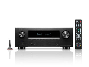 Ein schwarzer Denon AVR-X2800H DAB AV-Receiver (Schwarz) mit Display, zwei großen Drehreglern, Fernbedienung und Einmessmikrofon wird auf weißem Hintergrund gezeigt und hebt 8K-Videoqualität und Dolby Atmos-Unterstützung hervor.