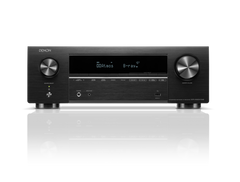 Ein Denon AVR-X1800H DAB AV-Receiver in Schwarz mit HEOS® Built-in, Frontdisplay mit Dolby Atmos und B-ray, großen Lautstärke-/Wahlschaltern, Steuertasten und Eingangsanschlüssen auf einer reflektierenden Oberfläche.