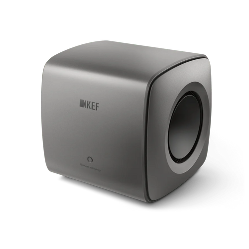 Der KEF KC62 Subwoofer in Titanium Grey besticht durch sein minimalistisches Design mit abgerundeten Kanten, einem Logo auf der Vorderseite und einem runden Seitenlautsprecher.
