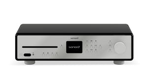 Der Sonoro Maestro Verstärker besticht durch sein modernes Design mit silberner Frontplatte, zentralem schwarzem Display, verschiedenen Tasten, CD-Einschub auf der linken Seite und einem großen Lautstärkeregler auf der rechten Seite.