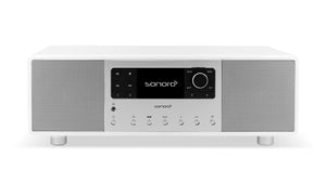 Ein Sonoro Primus in Weiß (hochglänzend)-Silber mit zentralem Digitaldisplay, großem Drehknopf, Tasten und zwei seitlichen Lautsprechergittern liefert ein unvergleichliches Hörerlebnis und 360°-Klangbild, frontal dargestellt vor einem schlichten weißen Hintergrund.