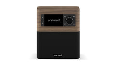 Das Sonoro Stream ist ein kompaktes Tisch-DAB+-Digitalradio im Walnuss-Dekor mit schwarzem Lautsprechergitter, Frontdisplay, Tasten und Wählscheibe. Das Sonoro-Logo erscheint sowohl auf dem Display als auch auf dem Gitter.